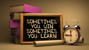 Sometimes You Win, Sometimes You Learn - Motivational Quote on Chalkboard with Hand Drawn Text, Stack of Books, Alarm Clock and Rolls of Paper on Blurred Background. Toned Image.